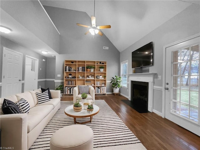 living area with baseboards, dark wood finished floors, ceiling fan, a fireplace with flush hearth, and high vaulted ceiling