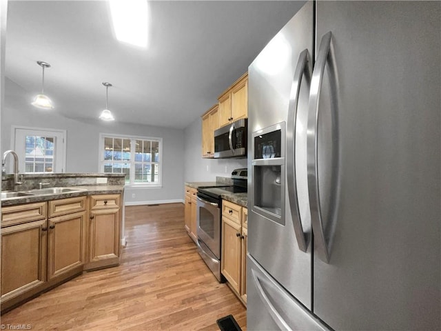 kitchen featuring a sink, appliances with stainless steel finishes, light wood finished floors, dark stone countertops, and pendant lighting