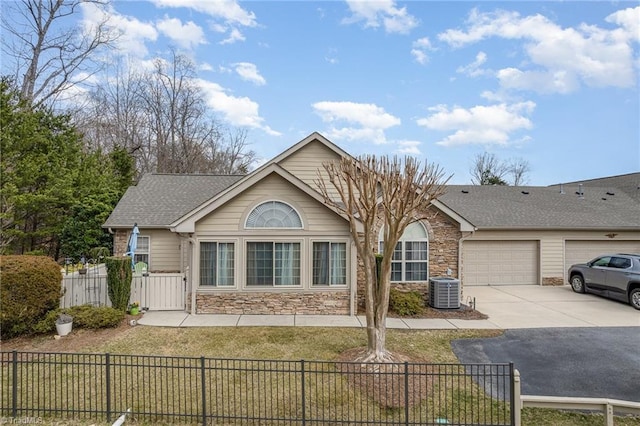 ranch-style house with a garage, stone siding, a fenced front yard, and driveway