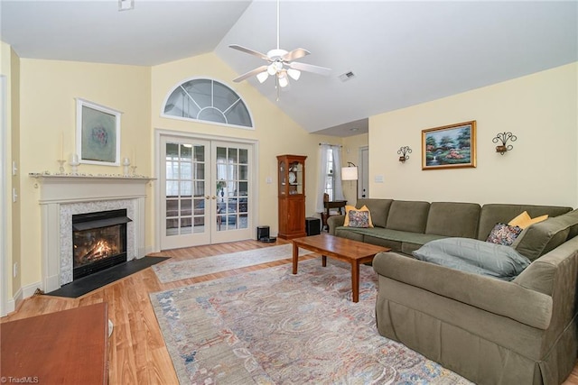 living room featuring visible vents, a ceiling fan, a fireplace with flush hearth, wood finished floors, and french doors