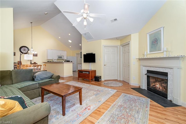 living area featuring visible vents, a premium fireplace, light wood-style floors, ceiling fan, and high vaulted ceiling