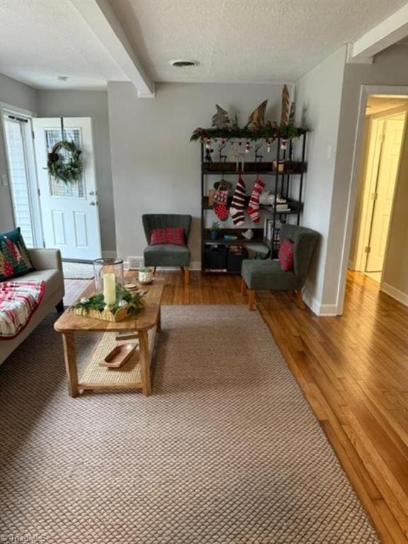 living room featuring beamed ceiling, a textured ceiling, and hardwood / wood-style flooring