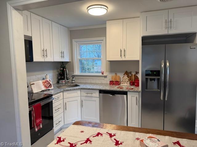 kitchen with light stone counters, ornamental molding, sink, black appliances, and white cabinets