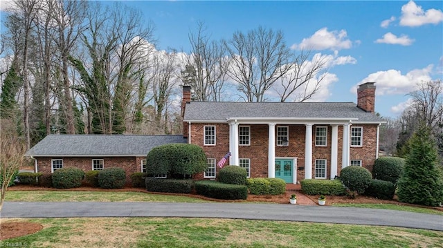 greek revival house featuring brick siding, a front yard, and a chimney