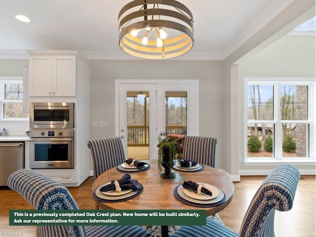 dining space with light wood-type flooring, french doors, a notable chandelier, and crown molding