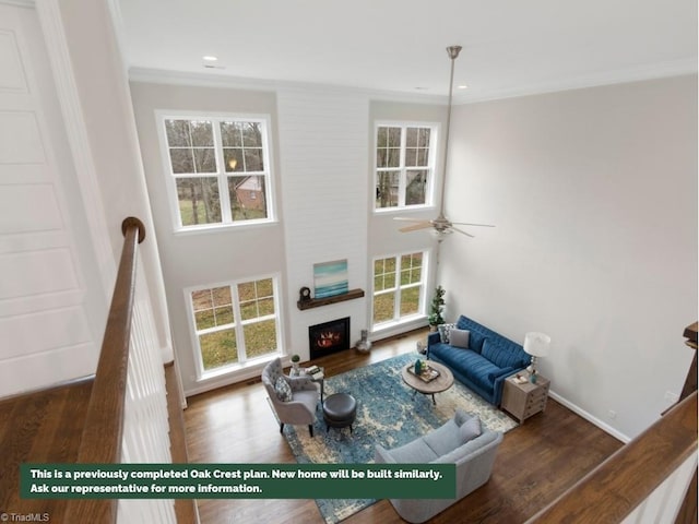 living room with ornamental molding, a wealth of natural light, a warm lit fireplace, and wood finished floors