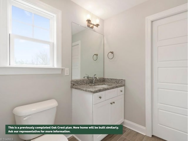 half bath featuring baseboards, vanity, and toilet