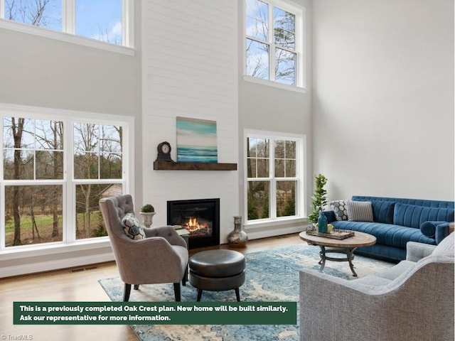 living room with a large fireplace, visible vents, a high ceiling, and wood finished floors