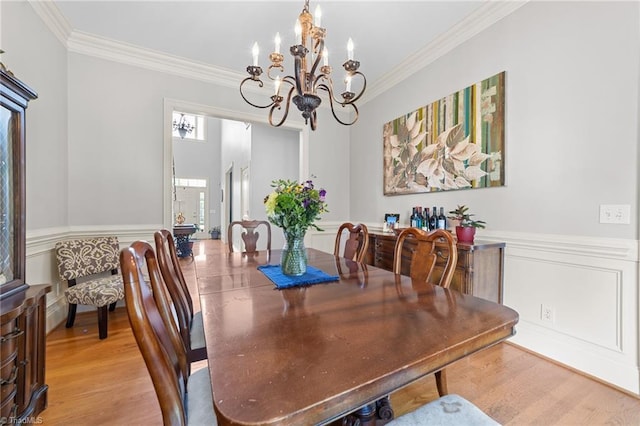 dining area featuring a wainscoted wall, ornamental molding, light wood-type flooring, and a chandelier
