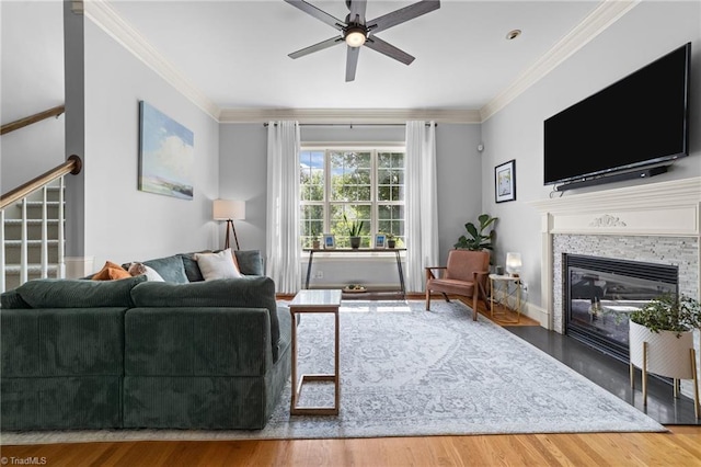 living area featuring ceiling fan, ornamental molding, a stone fireplace, and wood finished floors