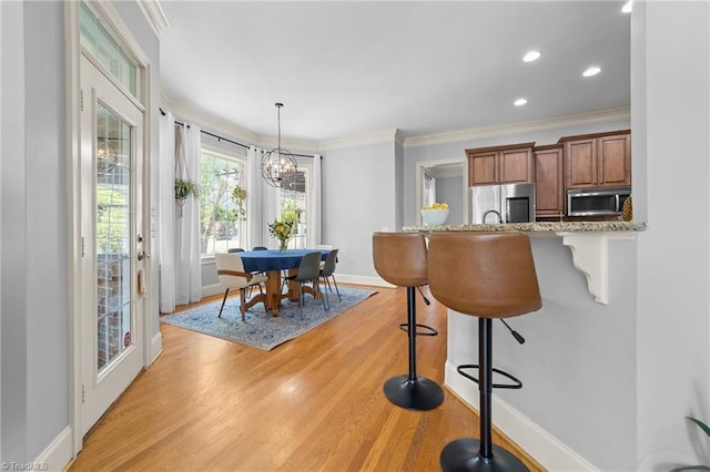 kitchen featuring brown cabinetry, crown molding, a breakfast bar area, light wood-style flooring, and stainless steel appliances