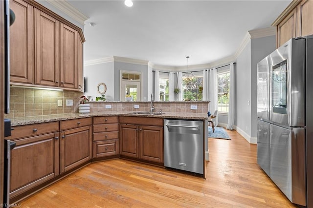 kitchen with a sink, brown cabinetry, stainless steel appliances, a peninsula, and ornamental molding