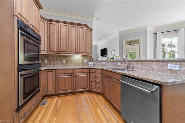 kitchen featuring brown cabinetry, a sink, light wood finished floors, and stainless steel appliances