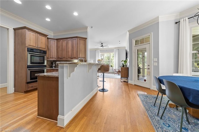 kitchen with light wood-style floors, stone countertops, a kitchen breakfast bar, stainless steel double oven, and brown cabinets