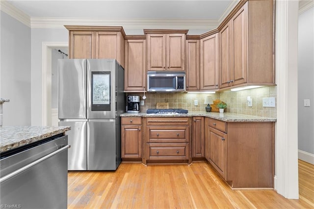 kitchen with brown cabinetry, light stone counters, light wood finished floors, backsplash, and stainless steel appliances