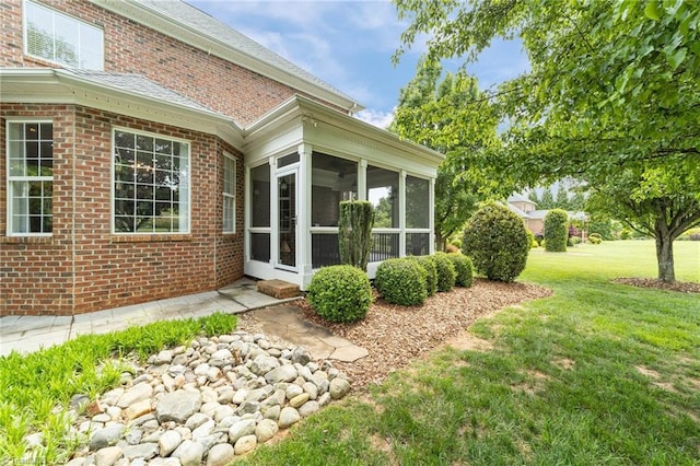view of side of property featuring brick siding, a yard, and a sunroom