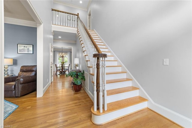 staircase featuring baseboards, ornamental molding, wood finished floors, and a notable chandelier