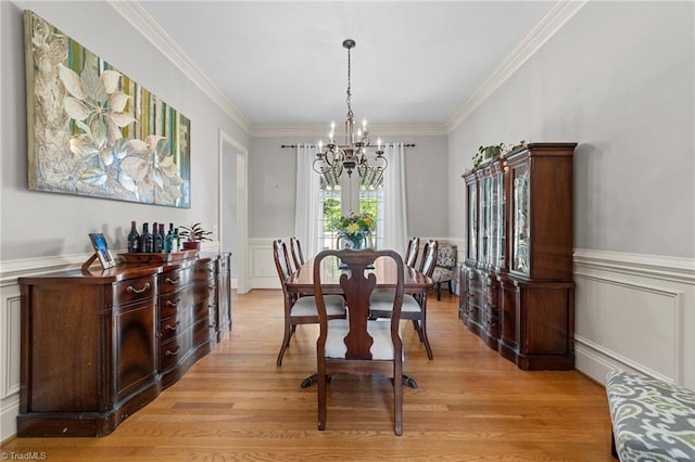 dining area with a wainscoted wall, a chandelier, ornamental molding, a decorative wall, and light wood-style flooring