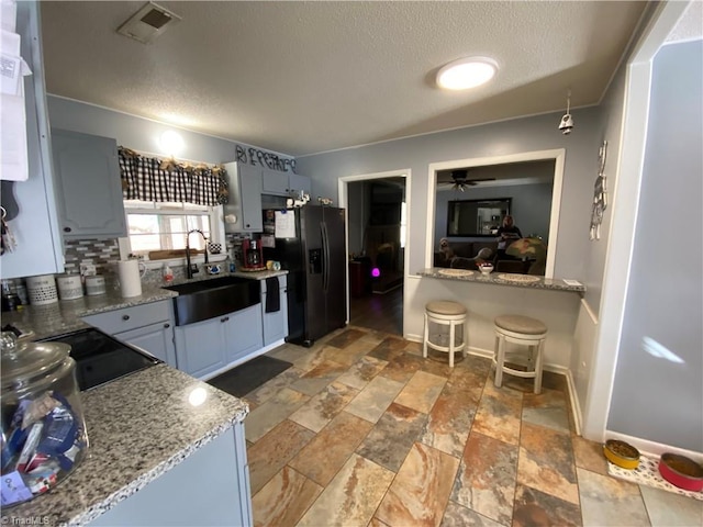 kitchen featuring black refrigerator with ice dispenser, sink, ceiling fan, and light stone counters