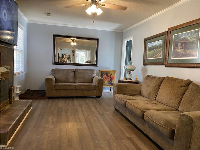 living room featuring ceiling fan, crown molding, a textured ceiling, a fireplace, and hardwood / wood-style flooring