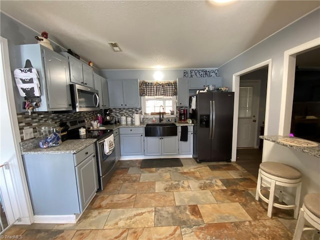 kitchen featuring light stone countertops, appliances with stainless steel finishes, gray cabinetry, and sink