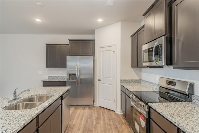 kitchen with appliances with stainless steel finishes, sink, light stone counters, dark brown cabinets, and light wood-type flooring