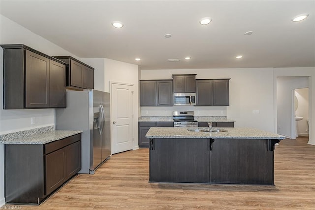 kitchen featuring stainless steel appliances, light stone countertops, sink, and a center island with sink