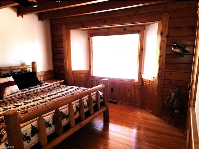 bedroom featuring beam ceiling, wooden walls, and hardwood / wood-style floors