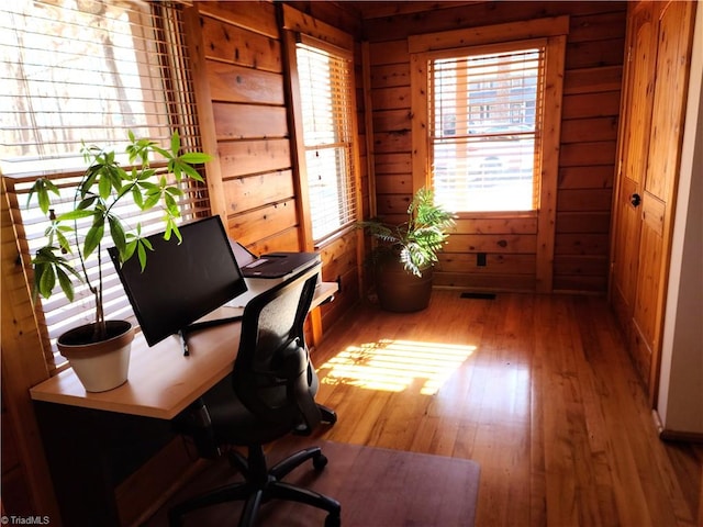 home office with light hardwood / wood-style floors and wooden walls