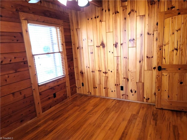 empty room featuring wood walls, ceiling fan, and wood-type flooring