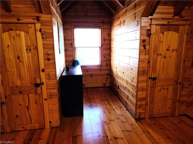 interior space featuring lofted ceiling with beams, light wood-type flooring, and wooden walls