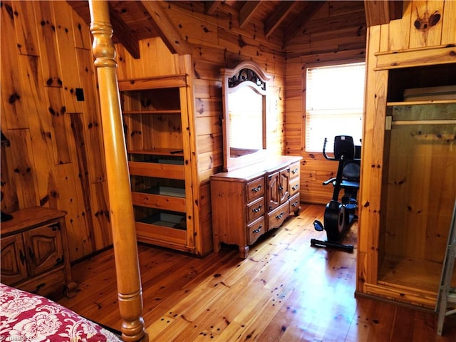 bedroom with vaulted ceiling with beams, wood walls, wood ceiling, and light hardwood / wood-style flooring