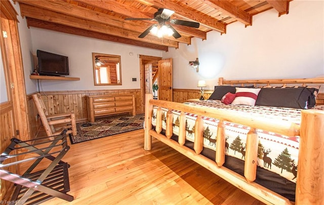 bedroom featuring beam ceiling, ceiling fan, wooden ceiling, wooden walls, and hardwood / wood-style flooring