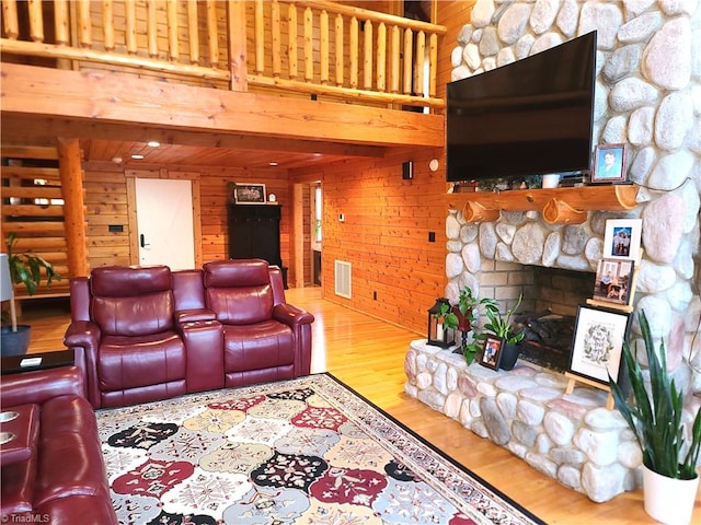 living room featuring a towering ceiling, light wood-type flooring, a stone fireplace, and wooden walls