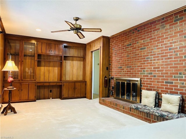 carpeted living area featuring a fireplace, a ceiling fan, ornamental molding, wood walls, and brick wall