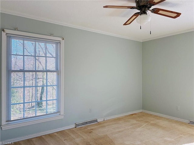 carpeted spare room with ornamental molding, a ceiling fan, visible vents, and baseboards