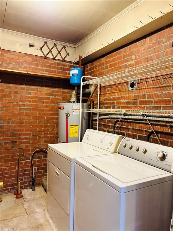 laundry room with laundry area, brick wall, water heater, and washer and clothes dryer