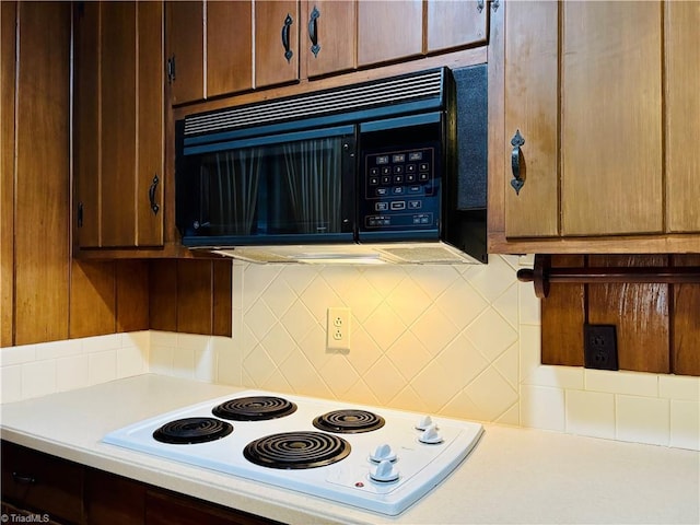 kitchen with tasteful backsplash, black microwave, light countertops, and white electric stovetop