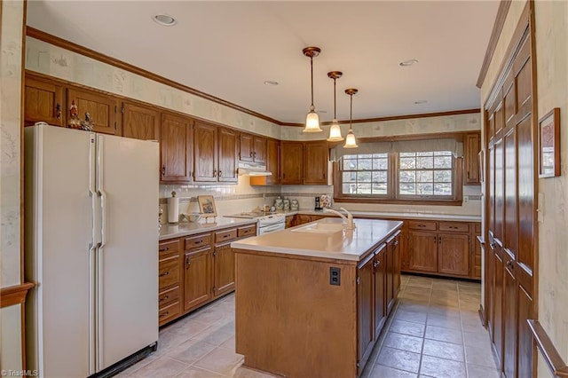 kitchen with decorative light fixtures, a center island with sink, light countertops, brown cabinetry, and white appliances