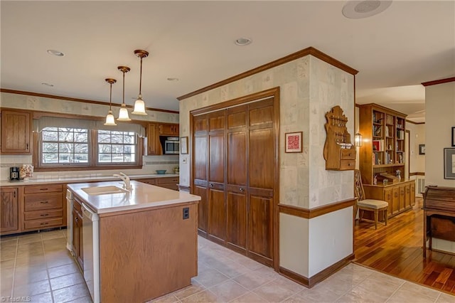 kitchen featuring a kitchen island with sink, a sink, light countertops, hanging light fixtures, and stainless steel microwave