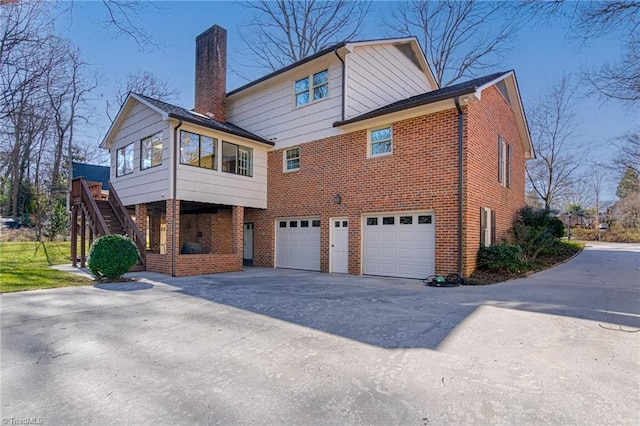 back of property featuring brick siding, a chimney, stairway, an attached garage, and driveway