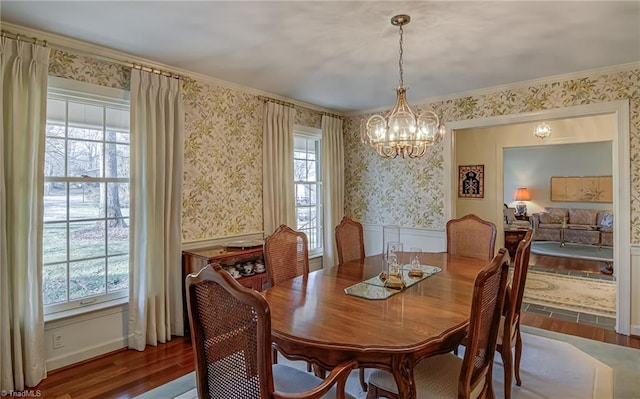 dining space with a chandelier, wood finished floors, crown molding, and wallpapered walls