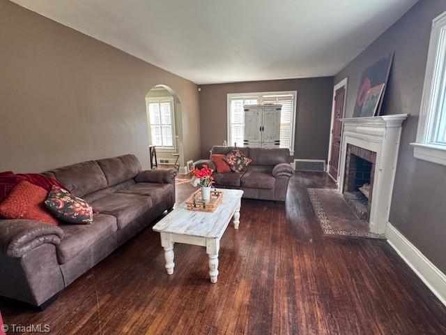 living room featuring baseboards, arched walkways, wood finished floors, and a fireplace