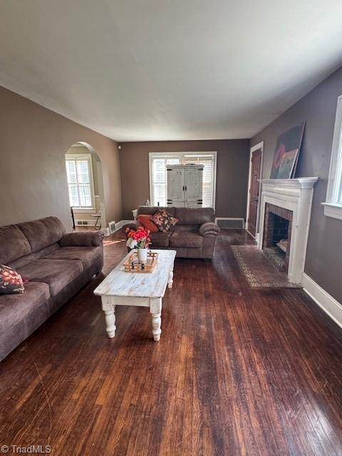 living area with a fireplace with raised hearth, baseboards, wood finished floors, and arched walkways
