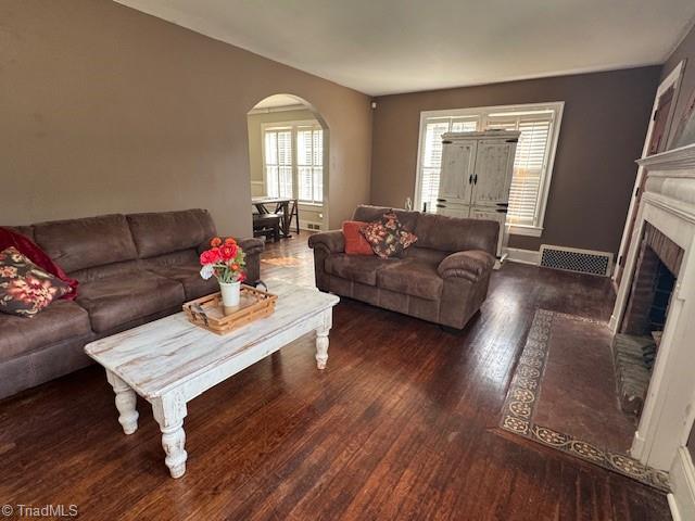 living room with arched walkways, visible vents, wood finished floors, and a fireplace
