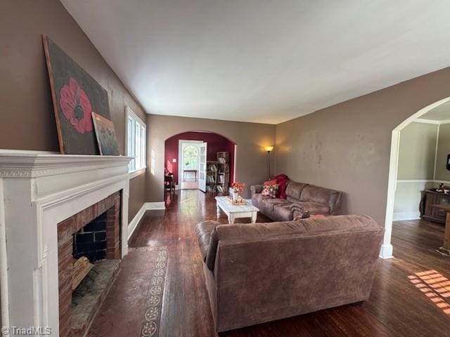living area with baseboards, arched walkways, wood finished floors, and a fireplace