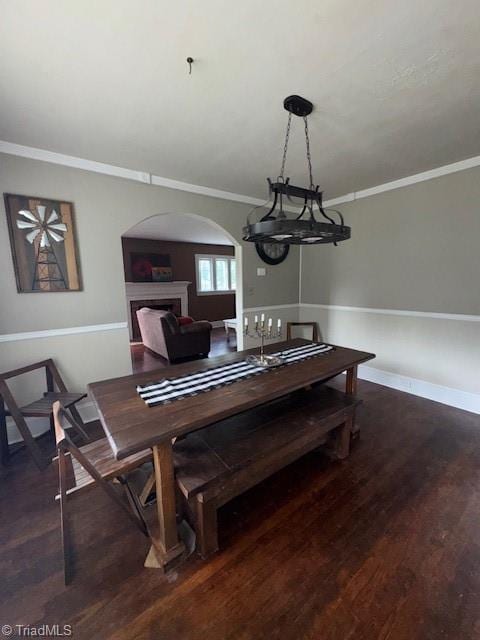 dining space with arched walkways, wood finished floors, a fireplace, and ornamental molding