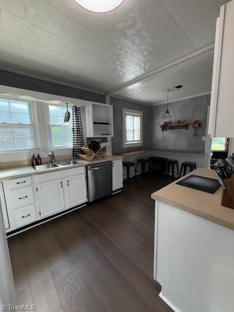 kitchen with stainless steel dishwasher, a sink, light countertops, dark wood-style floors, and white cabinetry