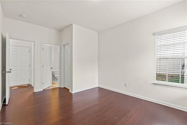 unfurnished bedroom featuring connected bathroom, dark wood-type flooring, and multiple windows