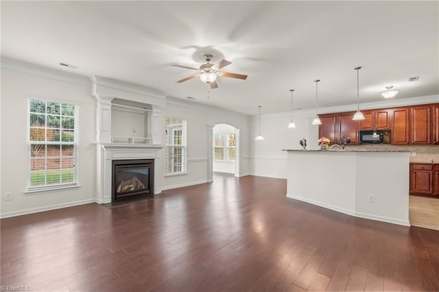 unfurnished living room featuring dark wood-type flooring, ceiling fan, crown molding, and plenty of natural light